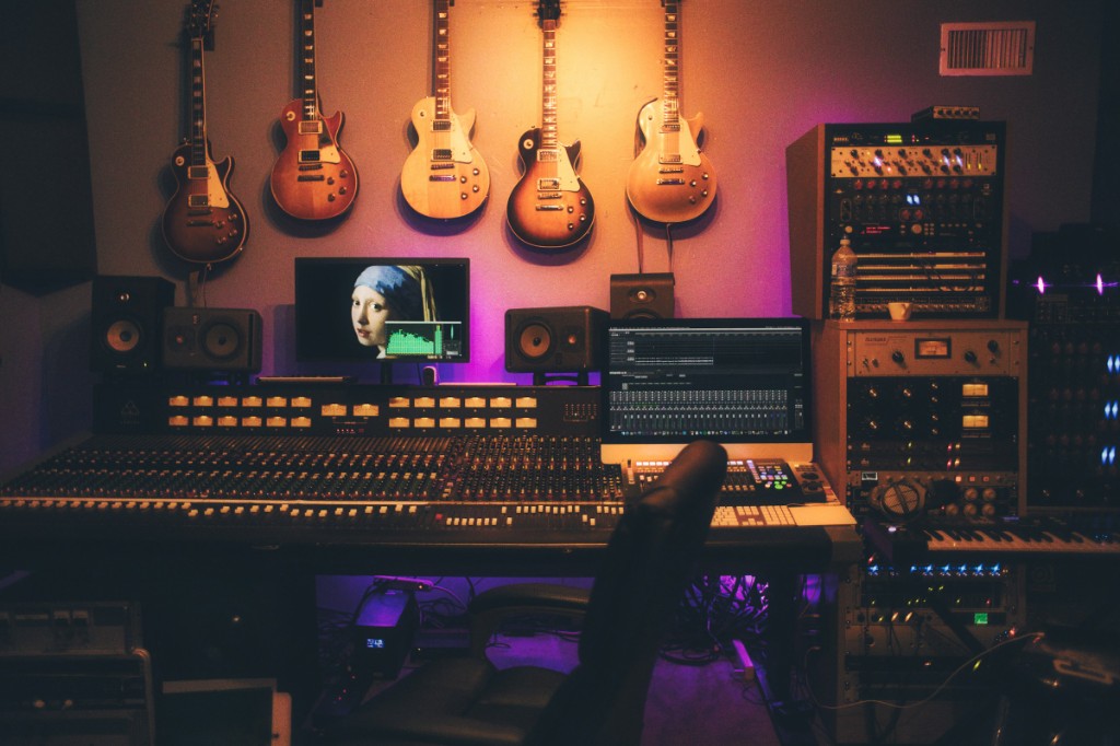 Mixing console with guitars on the wall, studio monitors, and a session open on screen